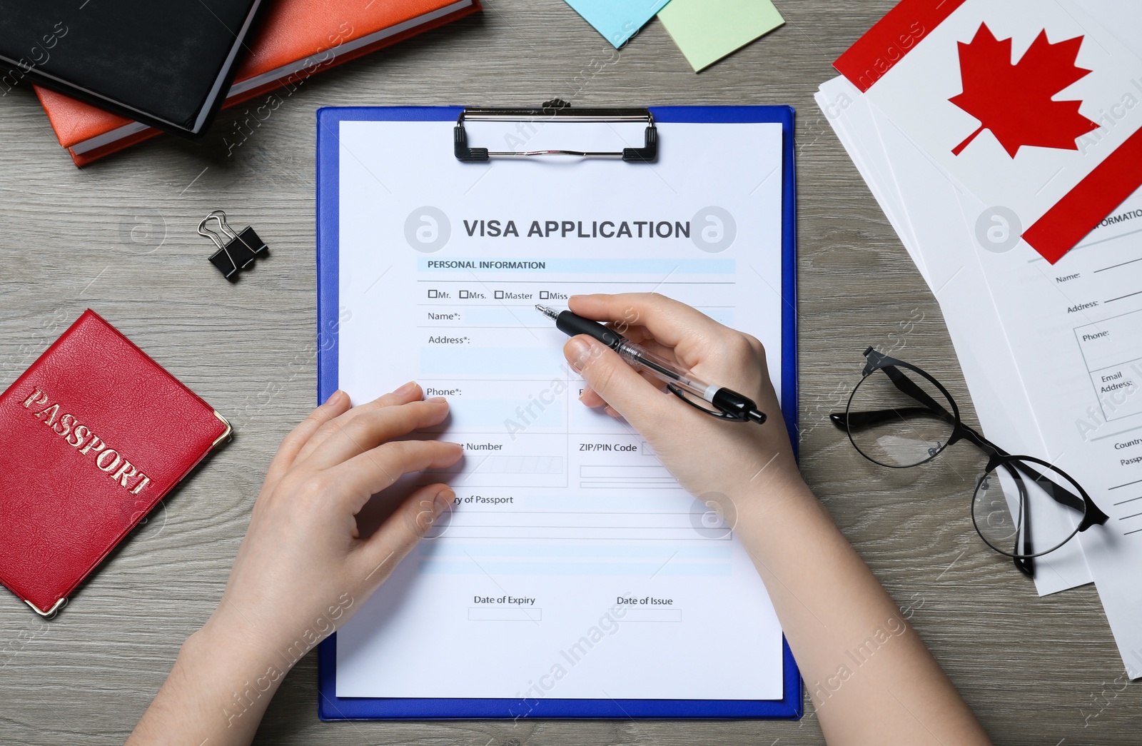 Photo of Woman filling visa application form to Canada at wooden table, top view