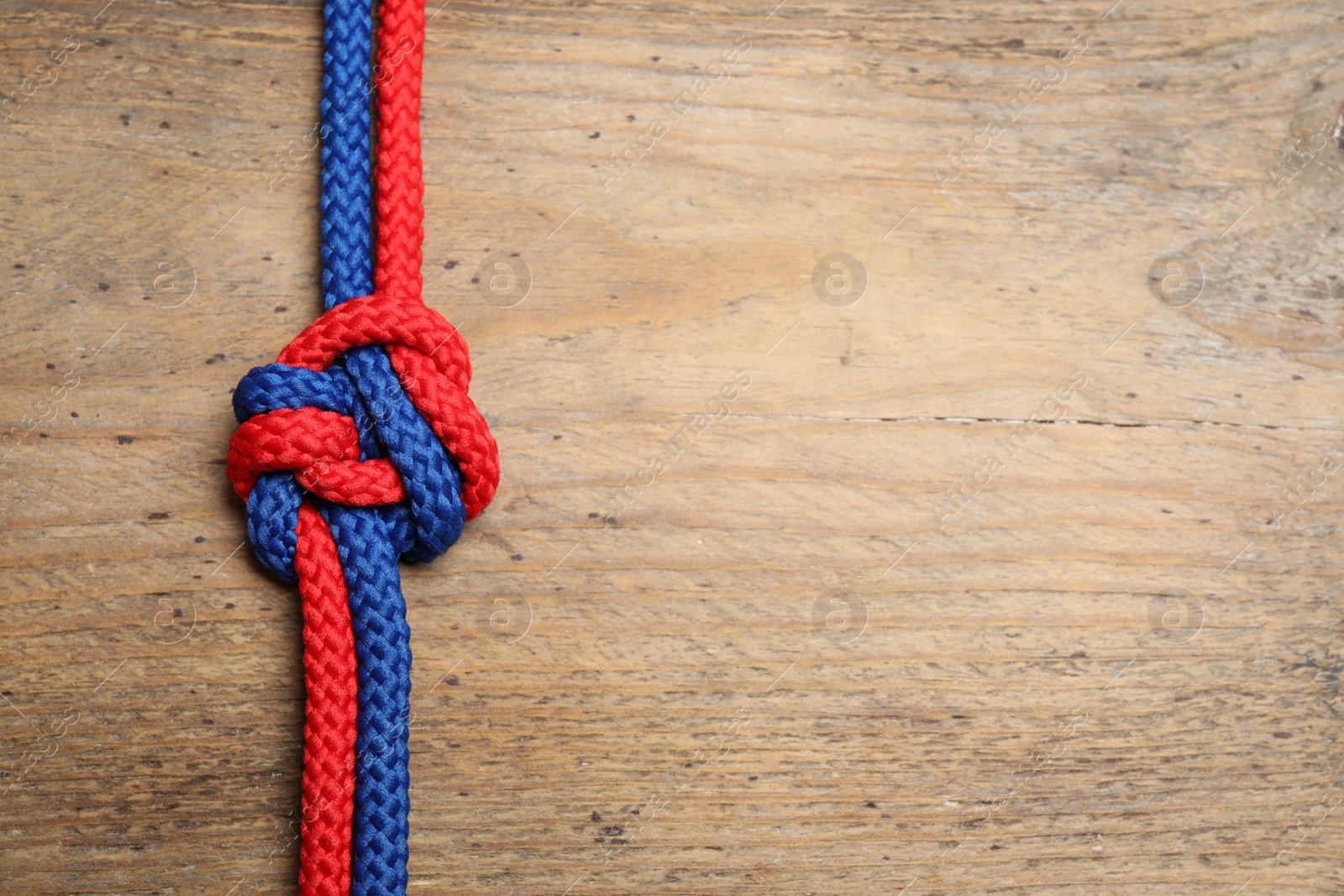 Photo of Top view of colorful ropes tied together on wooden background, space for text. Unity concept