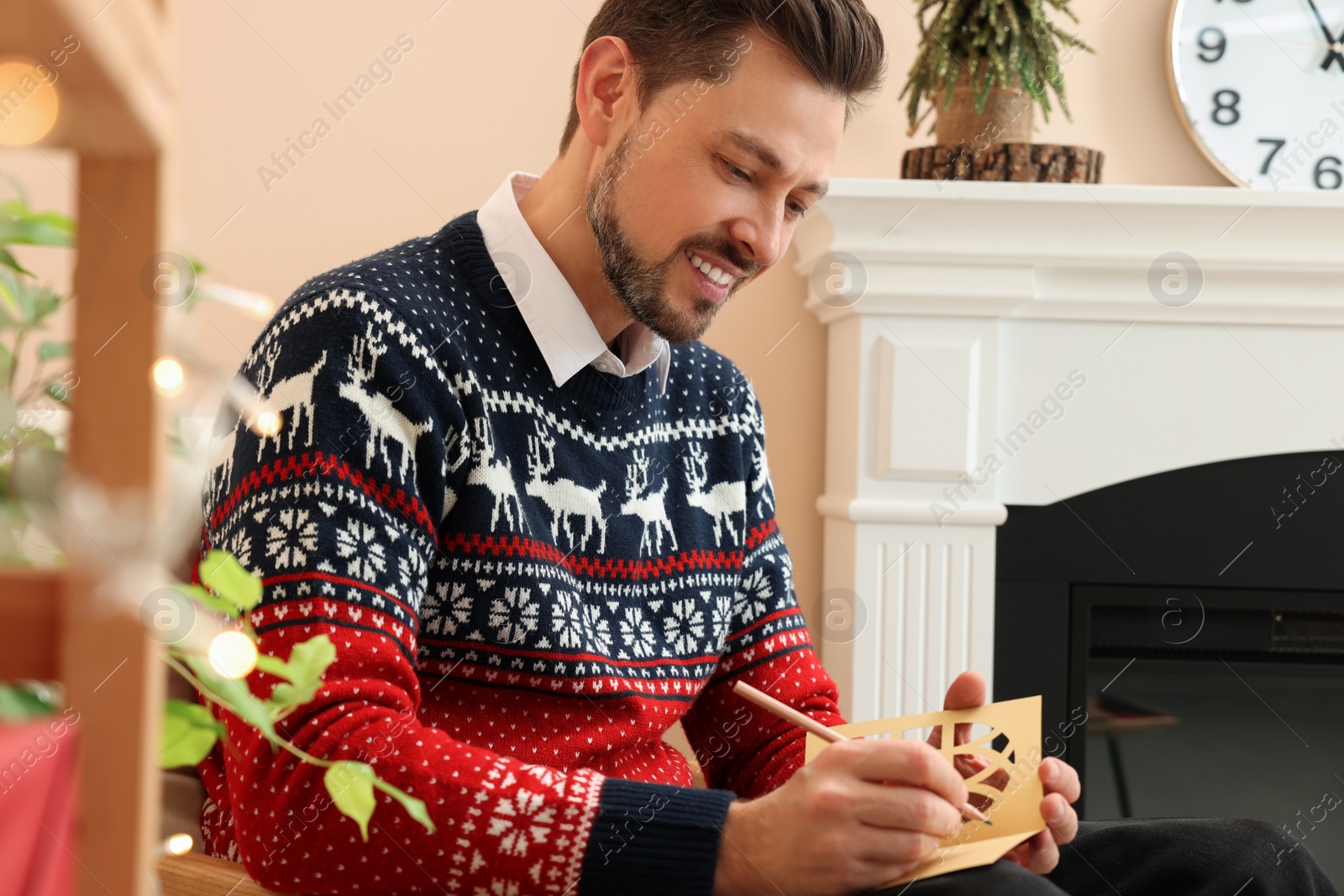 Photo of Happy man writing wishes in Christmas greeting card in living room