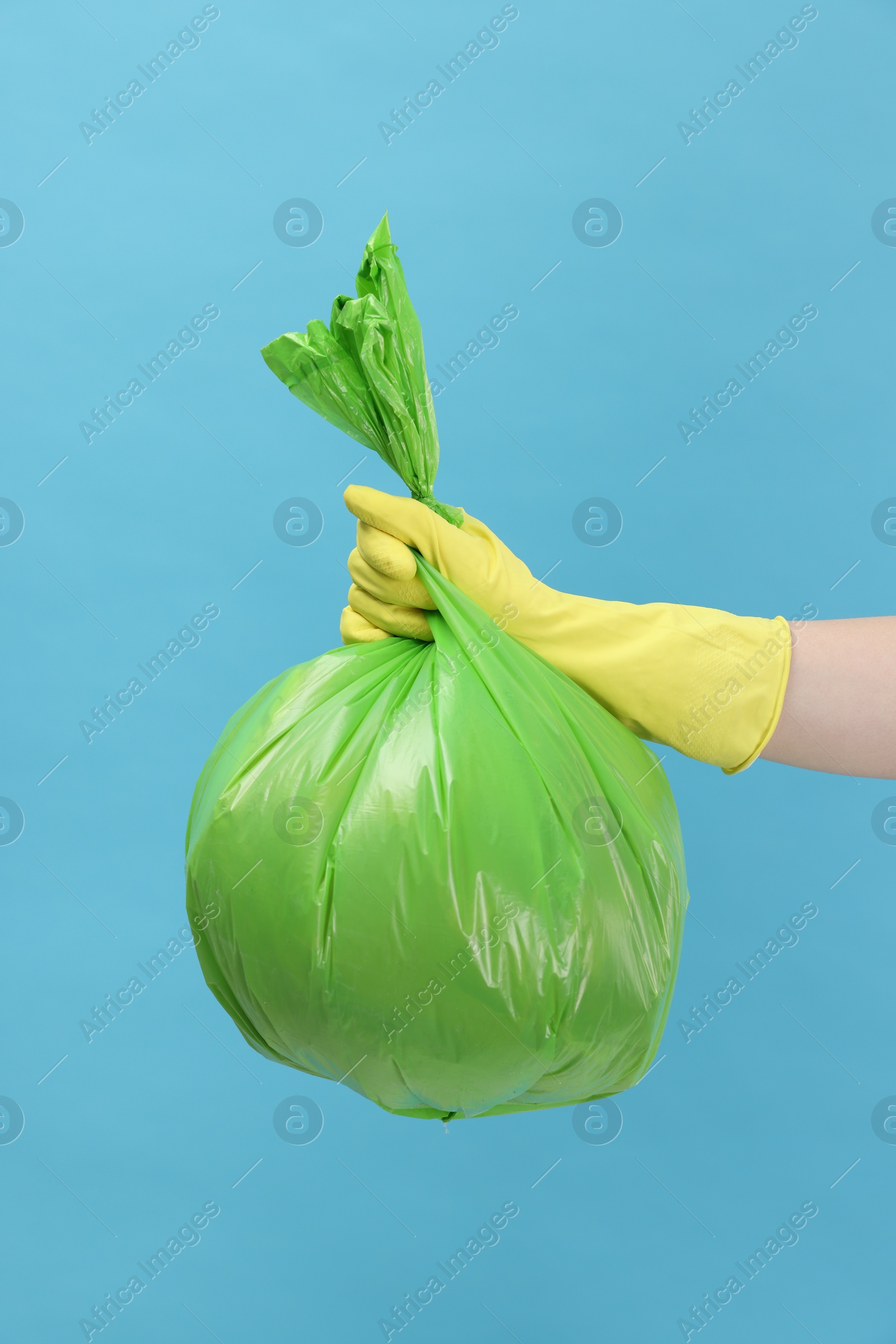 Photo of Woman holding plastic bag full of garbage on light blue background, closeup