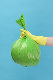 Photo of Woman holding plastic bag full of garbage on light blue background, closeup