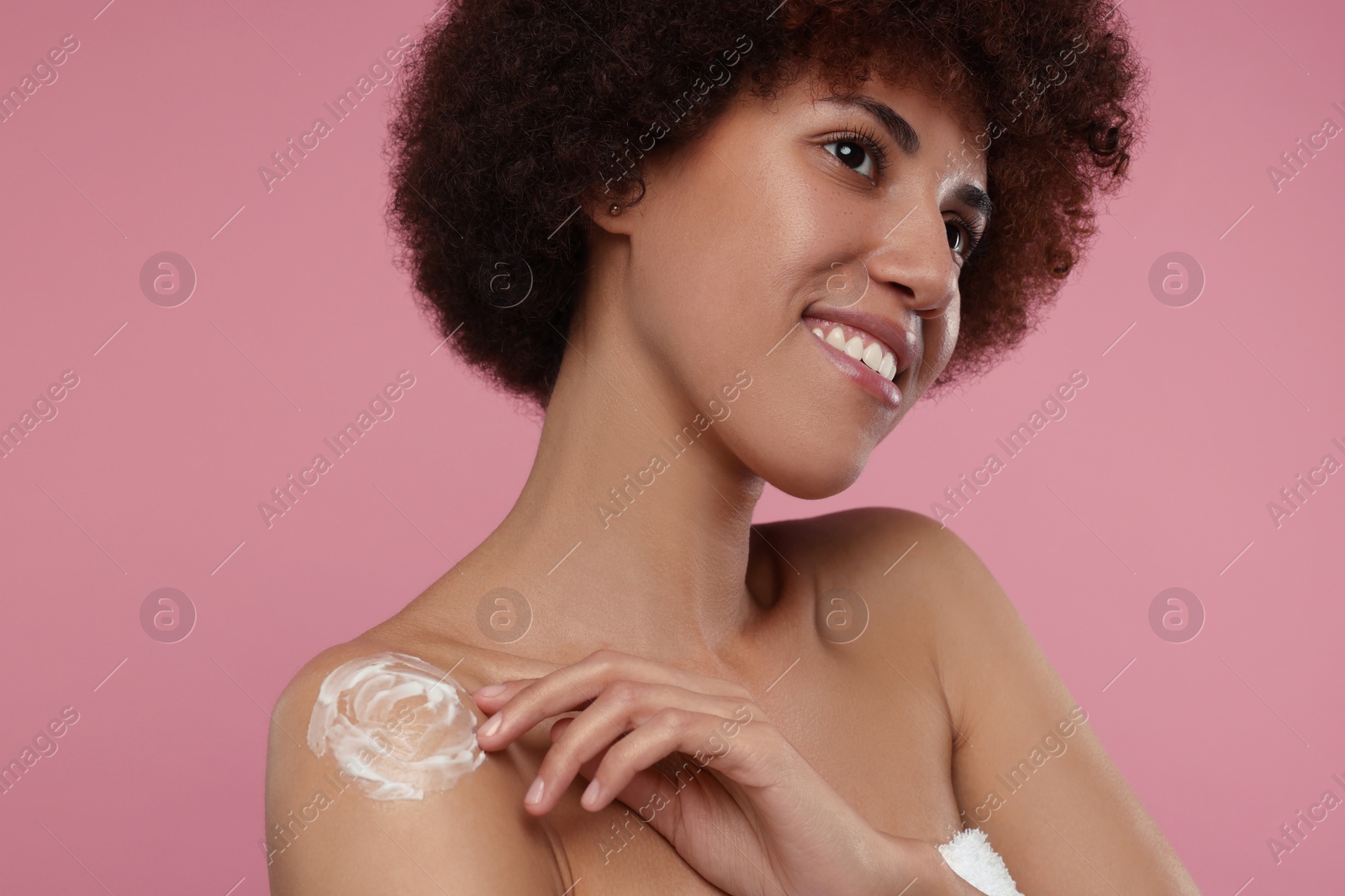 Photo of Beautiful young woman applying body cream onto shoulder on pink background