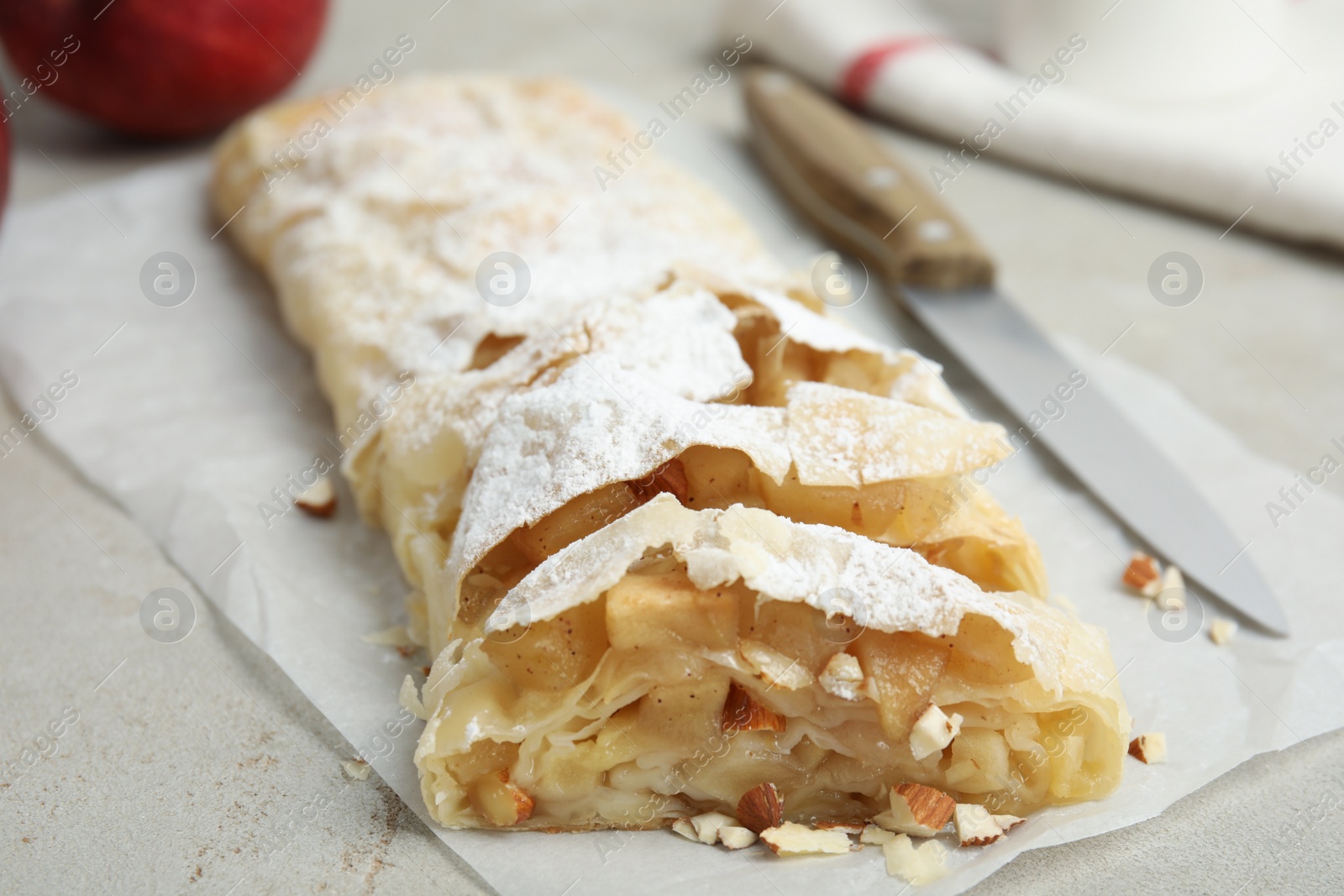 Photo of Delicious apple strudel with almonds and powdered sugar on light grey table, closeup