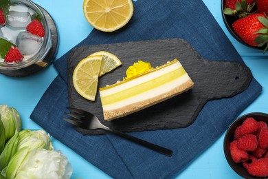 Photo of Delicious cheesecake with lemon, berries and peonies on light blue wooden table, flat lay