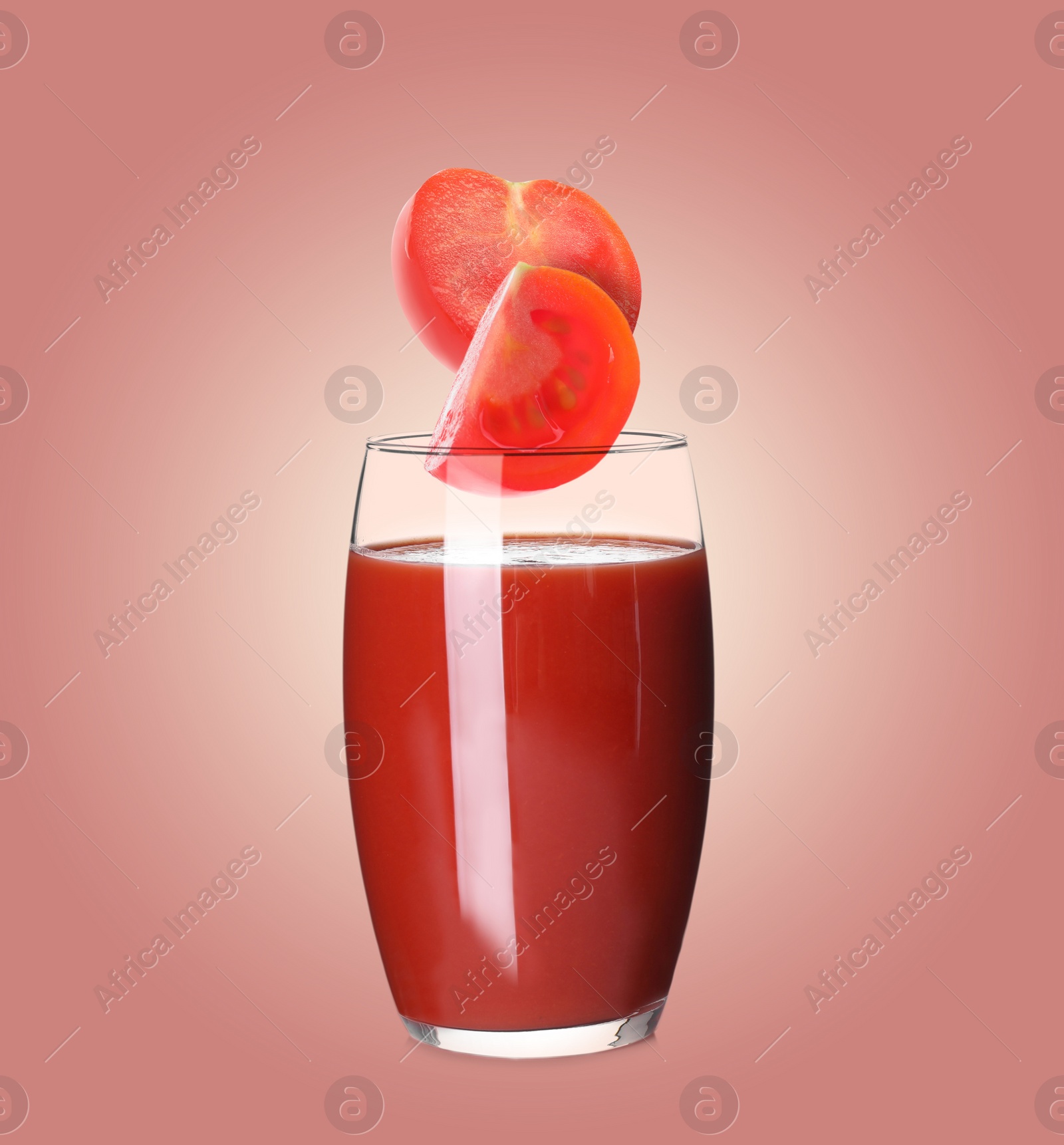 Image of Freshly made tomato juice on pale red background. Cut tomato falling into glass