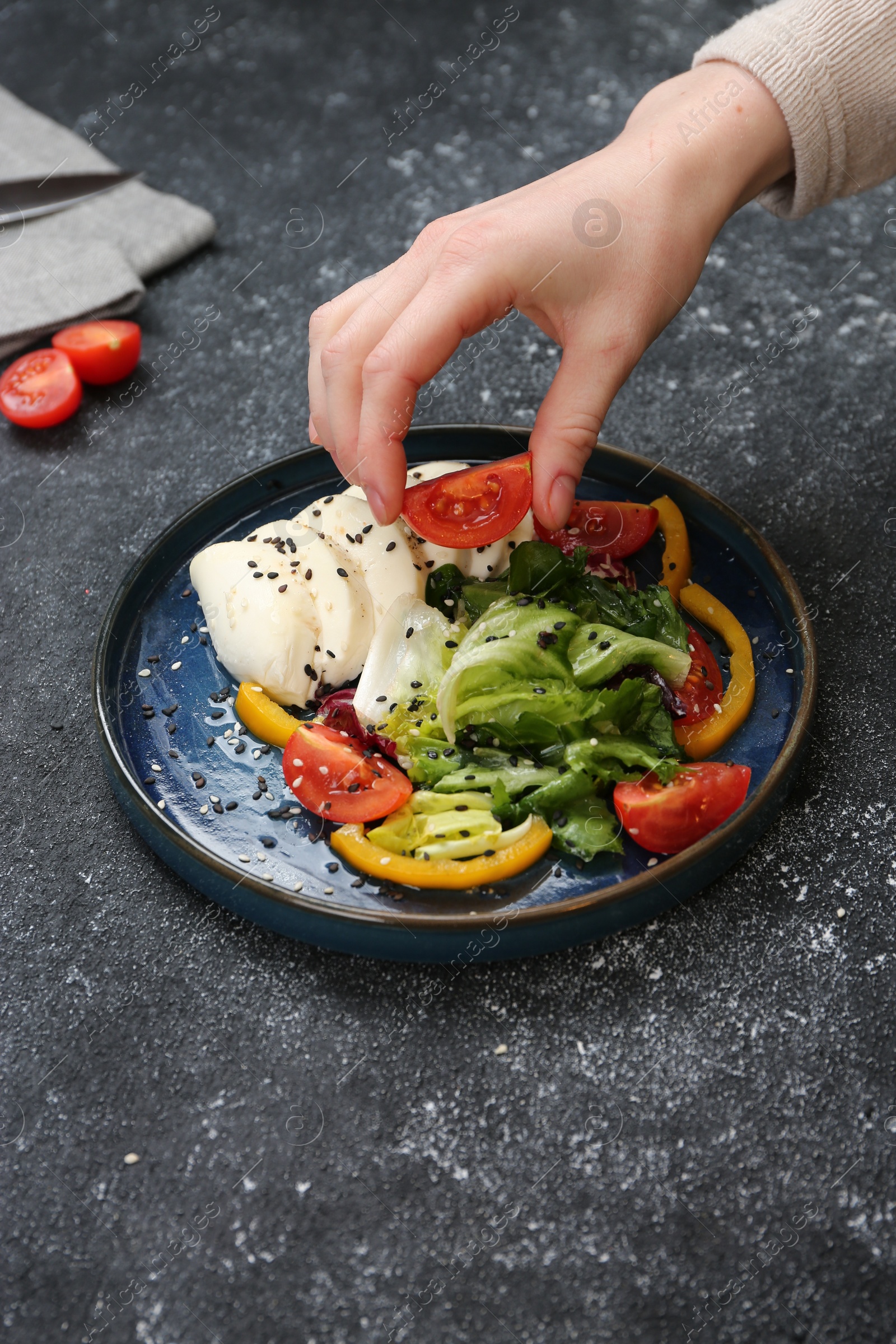 Photo of Food stylist preparing delicious salad with mozzarella and tomatoes for photoshoot at dark grey table in studio, closeup