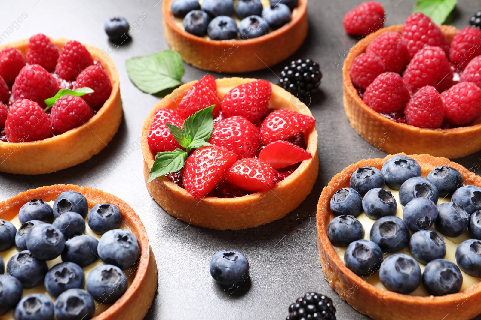 Photo of Tartlets with different fresh berries on grey table. Delicious dessert