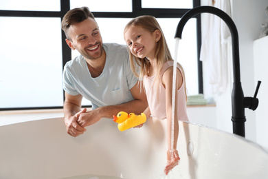 Photo of Father with his cute little daughter filling tub in bathroom