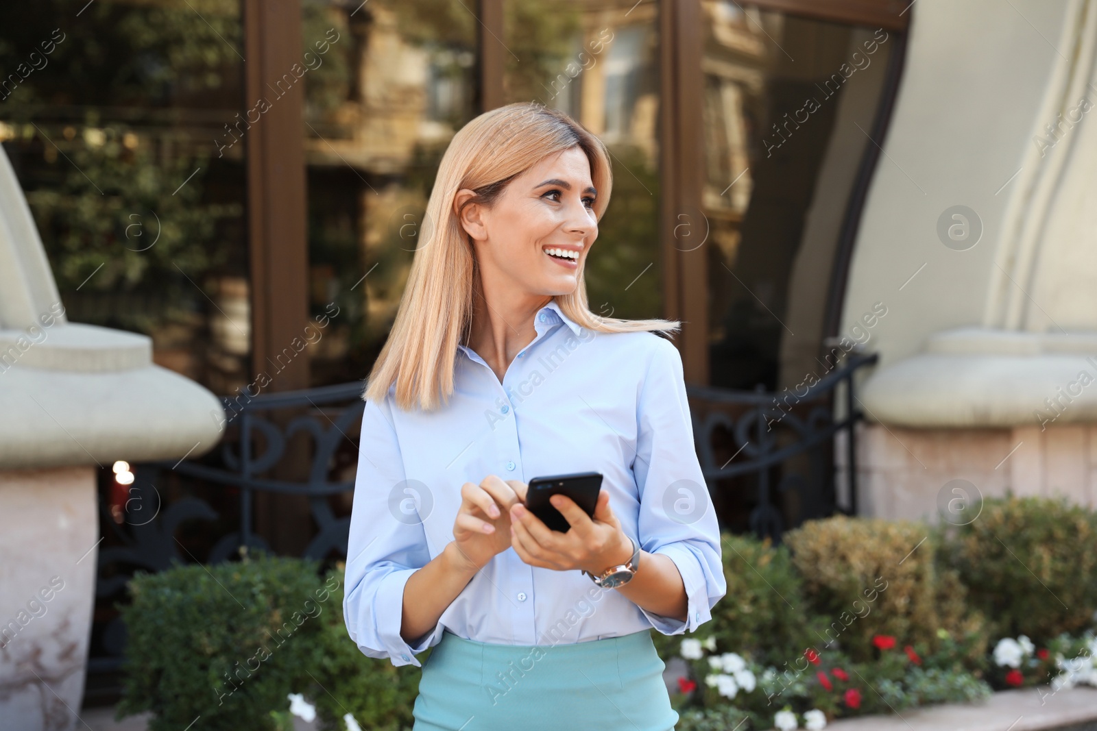 Photo of Female real estate agent with smartphone outdoors