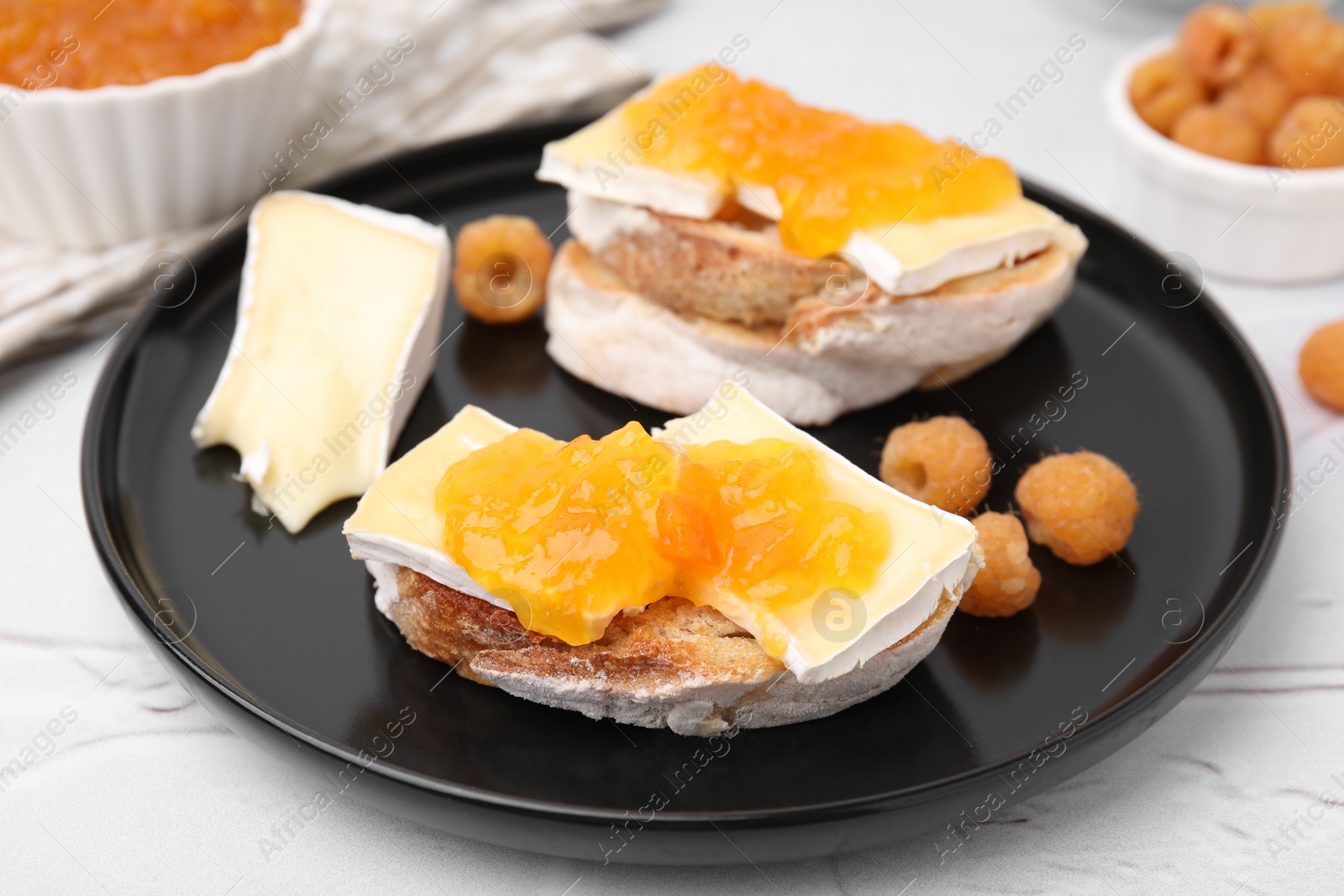 Photo of Tasty sandwiches with brie cheese, fresh raspberry and apricot jam on white table, closeup