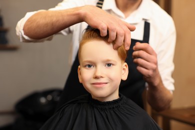 Photo of Professional hairdresser working with boy in beauty salon, closeup