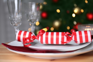 Photo of White plate with Christmas cracker on wooden table, closeup