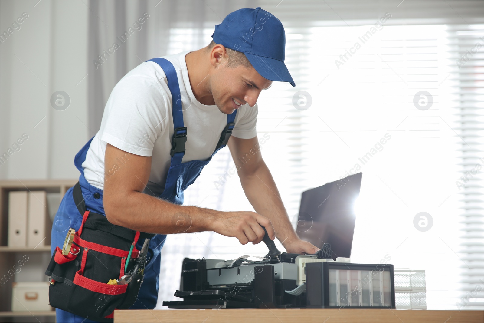 Photo of Repairman with screwdriver fixing modern printer in office