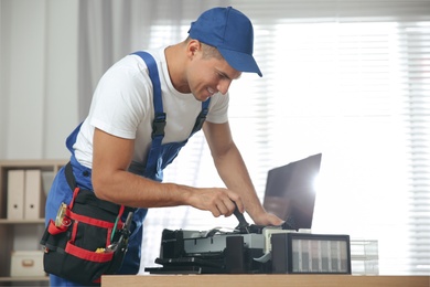 Repairman with screwdriver fixing modern printer in office