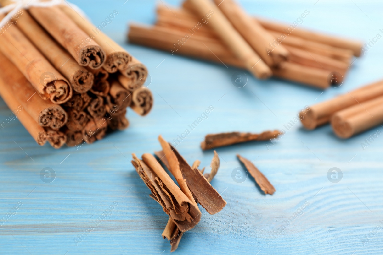 Photo of Aromatic cinnamon sticks on light blue wooden table, closeup