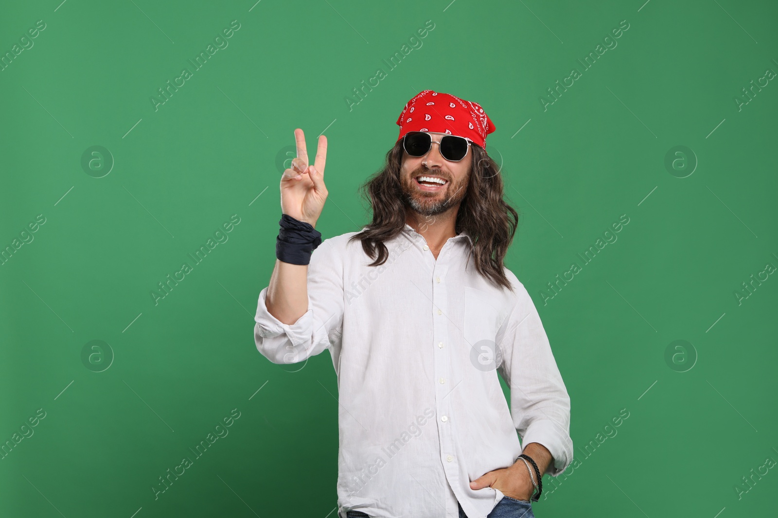 Photo of Stylish hippie man in sunglasses showing V-sign on green background