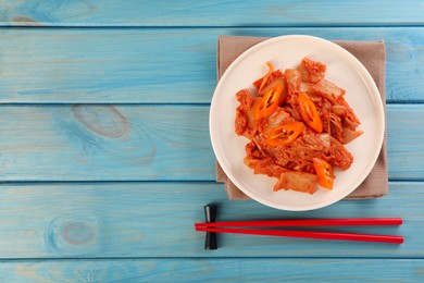 Photo of Plate of spicy cabbage kimchi with chili pepper and chopsticks on light blue wooden table, flat lay. Space for text