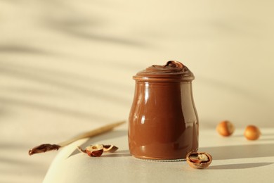 Glass jar with tasty chocolate hazelnut spread and nuts on white table