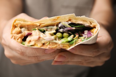 Woman holding delicious hummus wrap with vegetables, closeup