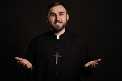 Priest wearing cassock with clerical collar on black background