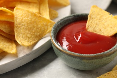 Photo of Tasty ketchup and tortilla chips on grey table, closeup