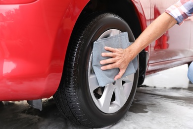 Photo of Man cleaning automobile wheel with duster, closeup. Car wash service