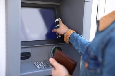 Photo of Young man using modern cash machine outdoors, closeup