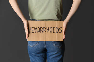 Woman holding carton sign with word HEMORRHOIDS on black background, closeup