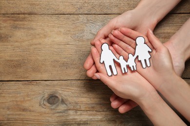 Photo of Couple holding paper family cutout at wooden table, top view. Space for text