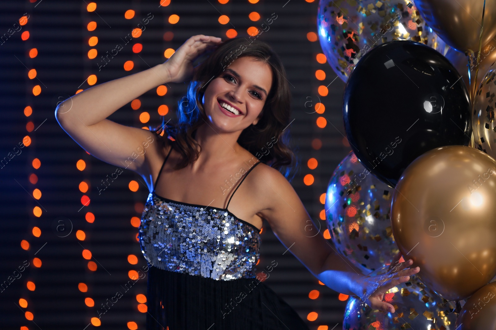 Photo of Happy woman with air balloons against blurred festive lights. Christmas party