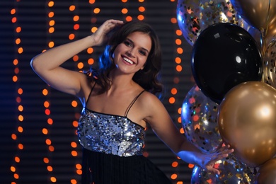 Photo of Happy woman with air balloons against blurred festive lights. Christmas party