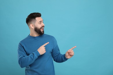 Happy young man with mustache pointing at something on light blue background. Space for text