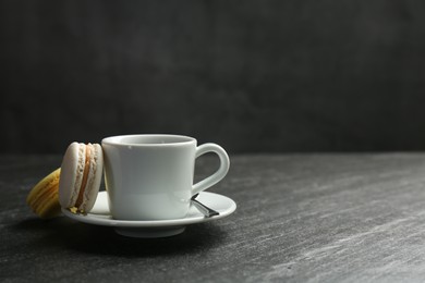 Photo of Hot coffee in cup, macarons and saucer on dark textured table. Space for text