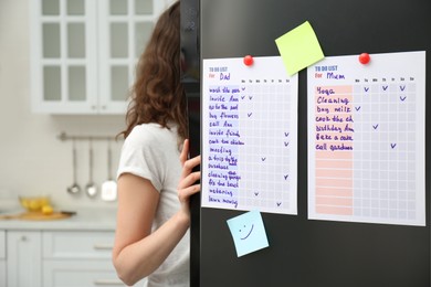 Woman near refrigerator with to do lists on door in kitchen
