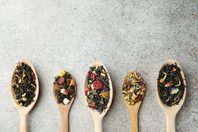 Photo of Different kinds of dry herbal tea in wooden spoons on light grey table, flat lay. Space for text
