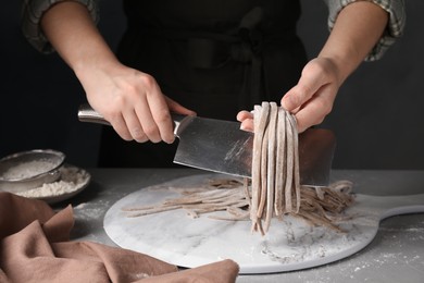 Photo of Woman making soba (buckwheat noodles) at grey table, closeup