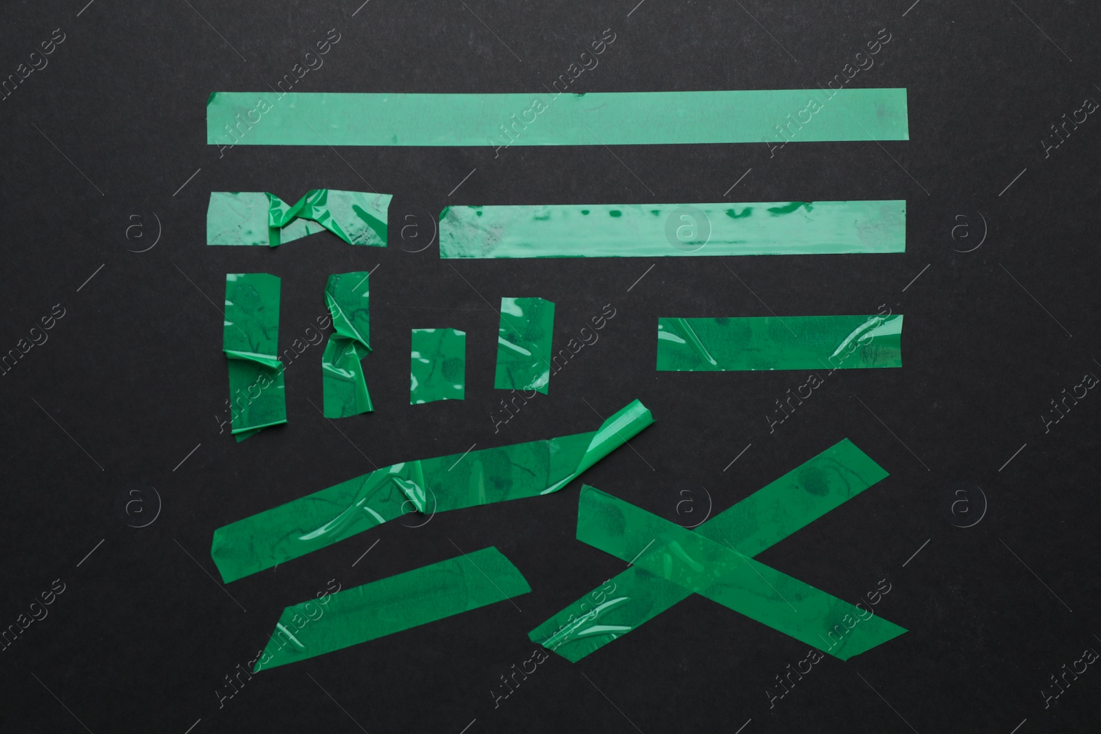 Photo of Many pieces of green adhesive tape on black background, flat lay