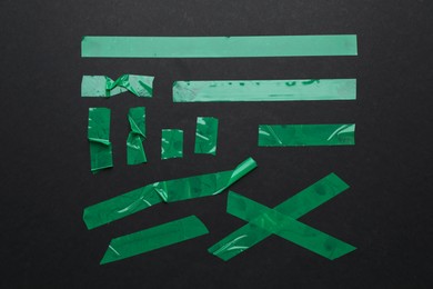 Photo of Many pieces of green adhesive tape on black background, flat lay