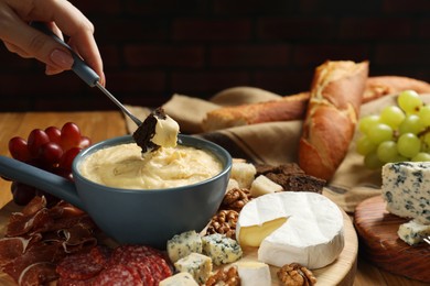 Woman dipping piece of bread into fondue pot with melted cheese at table, closeup