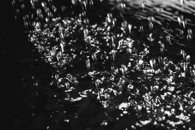 Photo of Heavy rain falling down on ground against dark background, closeup