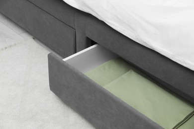 Photo of Storage drawer with bedding under modern bed in room, closeup