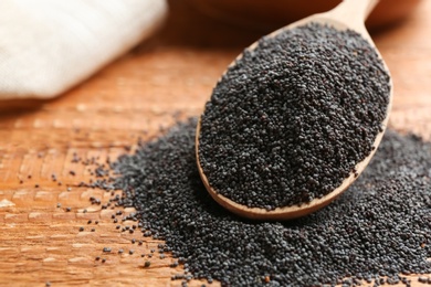 Photo of Poppy seeds and spoon on wooden table, closeup