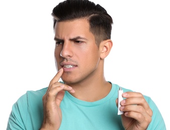 Photo of Emotional man with herpes applying cream on lips against white background