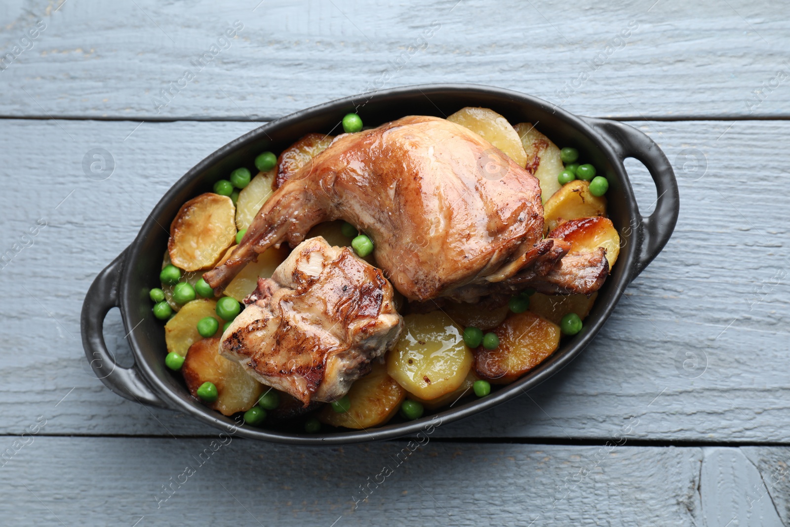 Photo of Tasty cooked rabbit with vegetables in baking dish on grey wooden table, top view