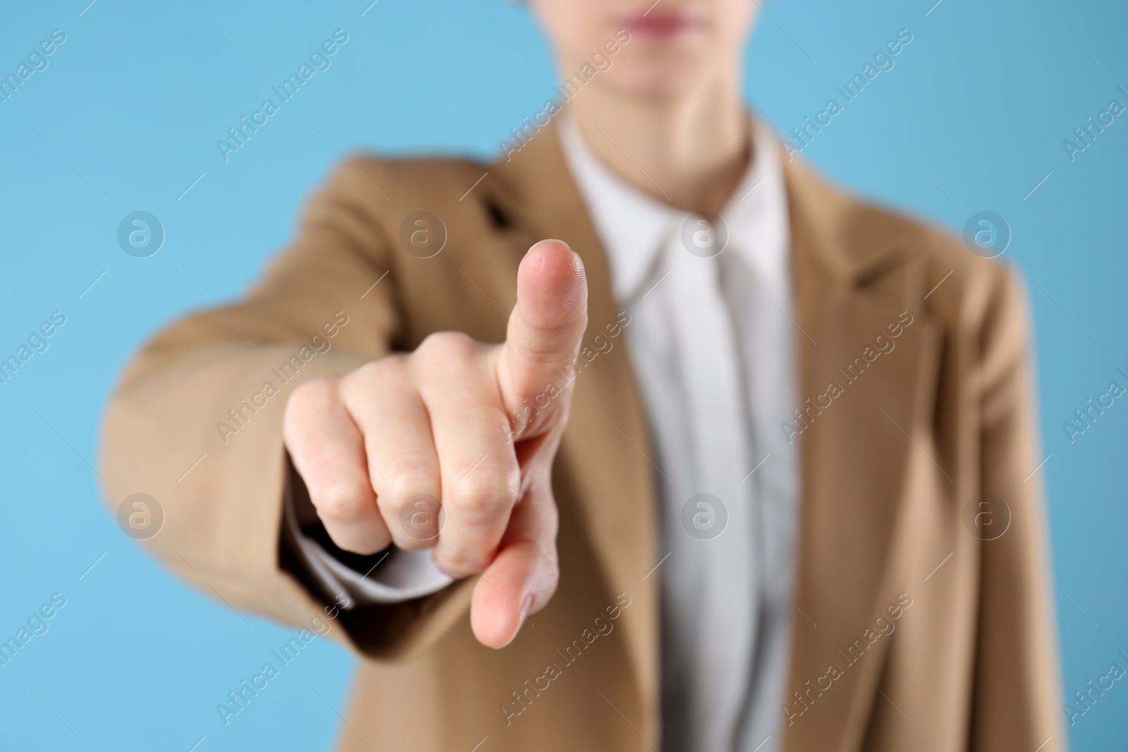 Photo of Businesswoman pointing at something on light blue background, closeup. Finger gesture