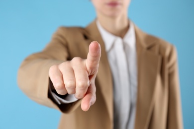 Businesswoman pointing at something on light blue background, closeup. Finger gesture