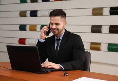 Salesman talking on phone at desk in car dealership