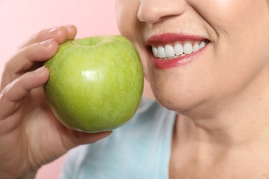 Smiling woman with perfect teeth and green apple on color background, closeup