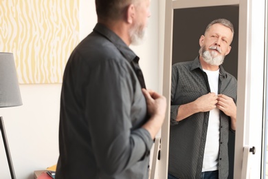 Photo of Mature man looking in mirror at home