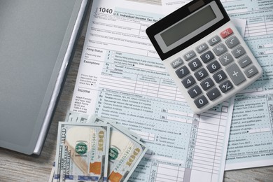Photo of Payroll. Tax return forms, calculator and dollar banknotes on wooden table, flat lay
